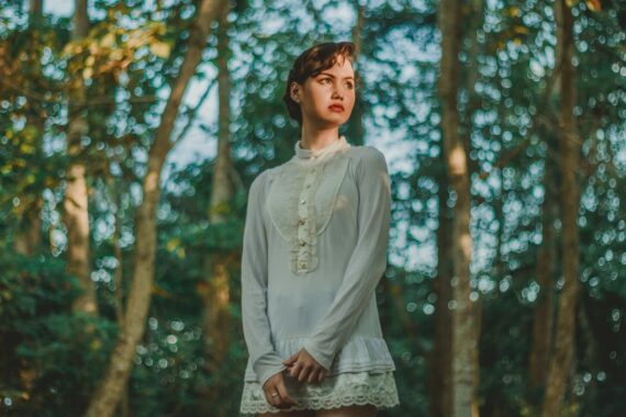 woman-in-white-long-sleeved-mini-dress-standing-under-trees